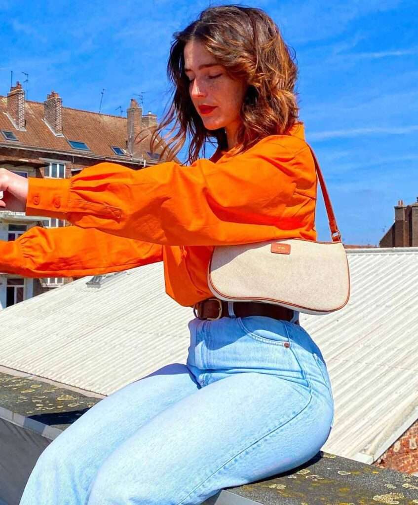 Alice in a orange dress shirt with reformation jeans while closing her eyes