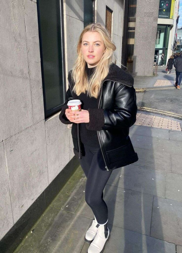 Annie Knowles is wearing a black jacket pair with matching high neck shirt, leggings and white joggers while holding a cup of coffee in her hand