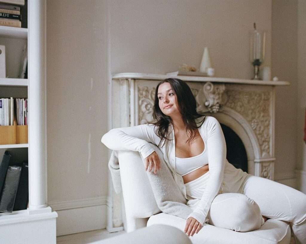 Kelsey Kotzur  in a stunning white 2 piece legging set while sitting on a sofa and poses for a picture
