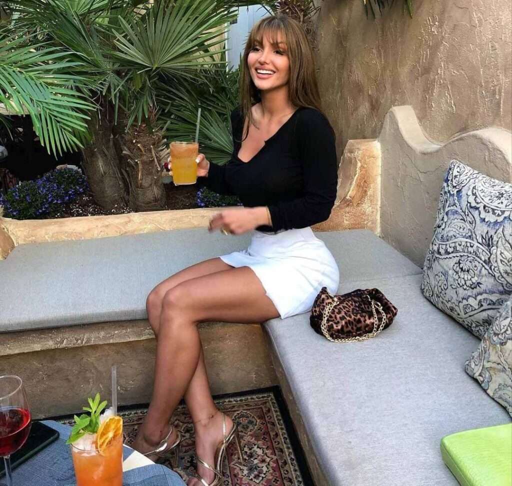 Stella-Marshall in a black fulls sleeves shirt with white shorts while holding a glass of fresh juice in her hand