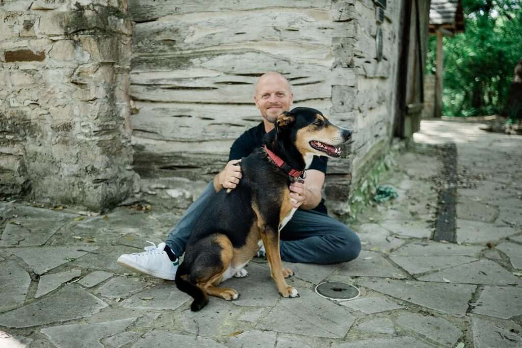 Trim Ferriss taking picture with his pet dog while wearing a black t-shirt with jeans