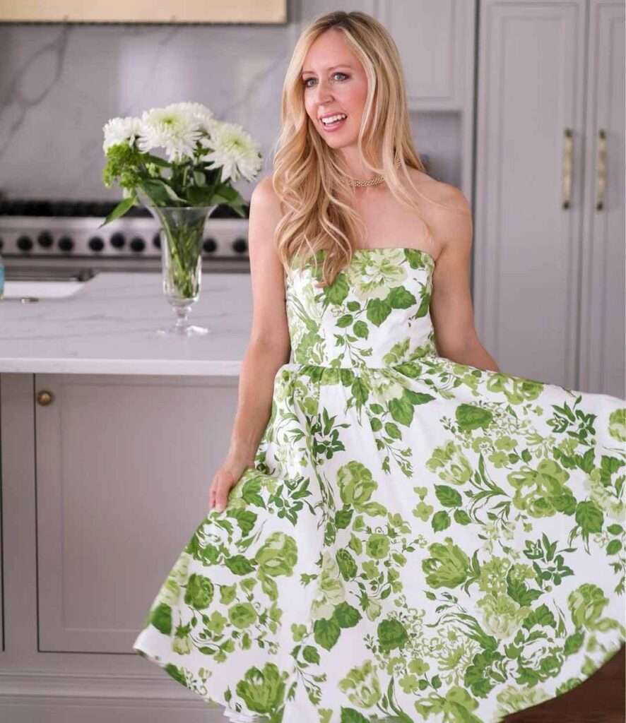 Tara is wearing a reformation style dress with green floral print while poses for a picture