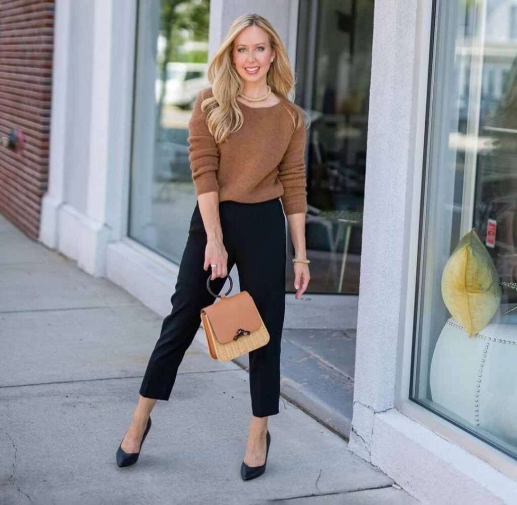 Tara in a dark brown full sleeves shirt pair with black pants, pumps, and a brown bag while smiling towards camera for a picture
