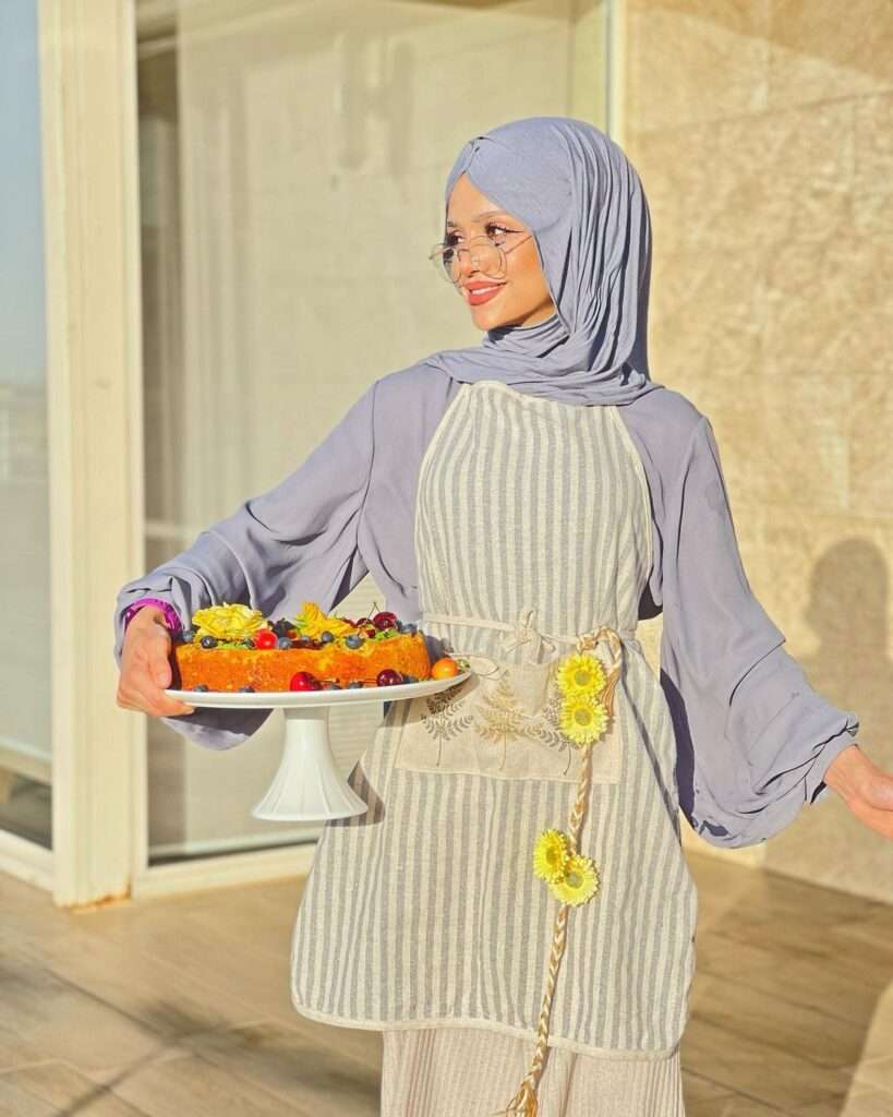 Abir-El-Saghir in a grey outfit while holding a cake in her hand and giving a side pose towards camera