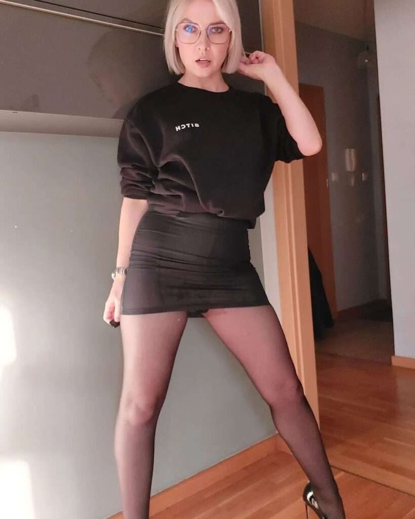 Alexandra in a black sweat shirt with a matchinh skirt and black pantyhose while looking towards camera