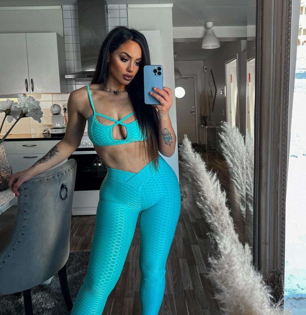 Antelainta-DH. in a blue crop striped top with leggings while taking a selfie in the front of mirror