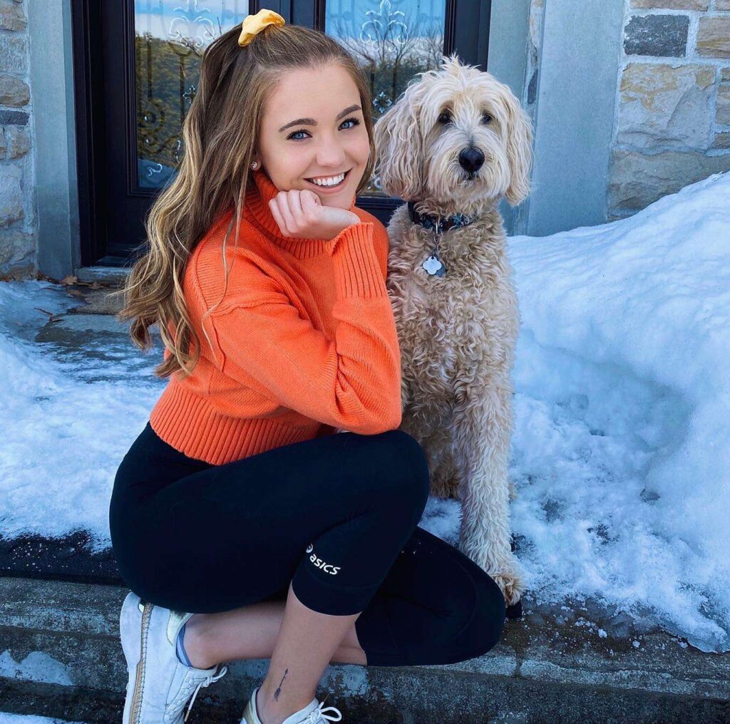 Charlotte Robillard in the orange shirt pair with black leggings and white shoes while taking photo with her pet