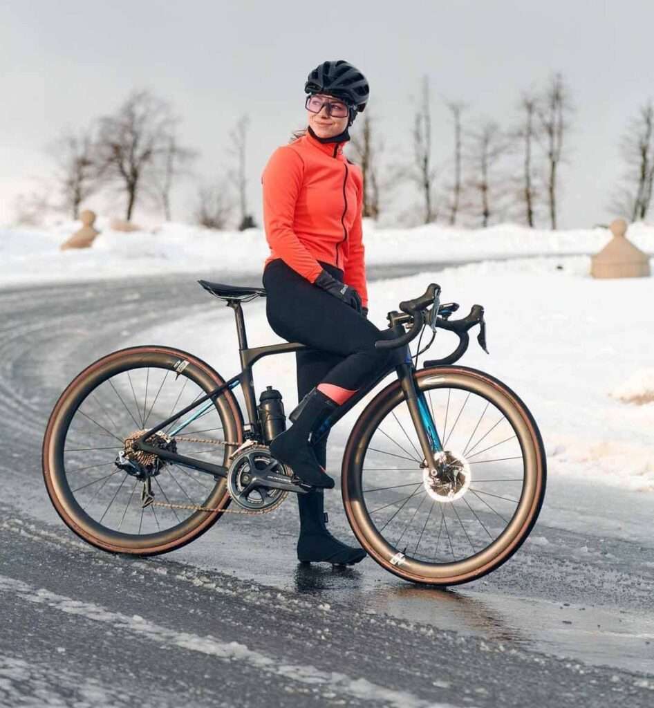 Marta-Swiatlon in orange full sleeves front zip shirt pair with black leggings and boots, wearing a helmet and sitting on the cycle