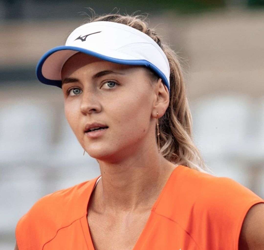 Maryna Zanevska wearing an orange shirt and white cap while taking a picture