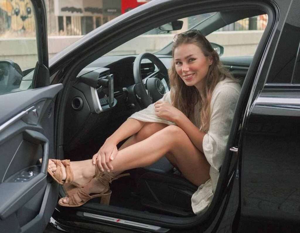 Puck Moonen in a reformation style dress, while sitting in a car and smiling towards camera