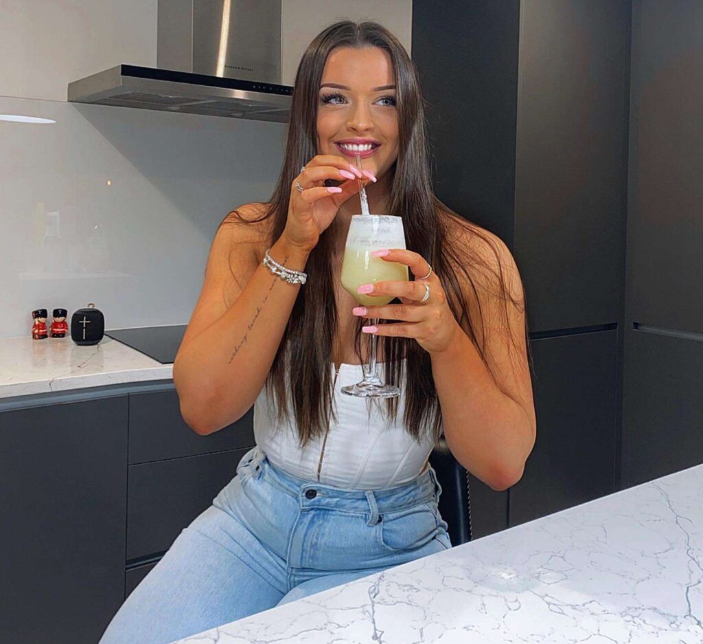 Tui jones in a white off shoulder top pair with blue jeans while drinking fresh juice