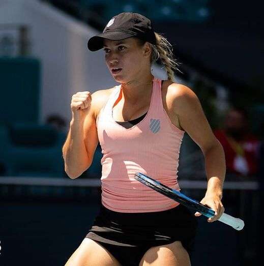 Yulia Putintseva in a pink tank top with black shorts while holding a racket in her hand in the tennis court