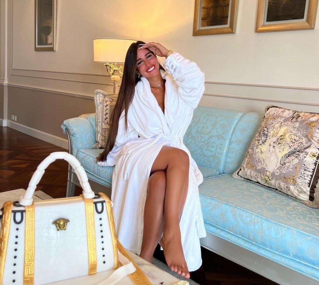 Avital Cohen in a white bathroba while sitting on the sky blue sofa while smiling towards the camera