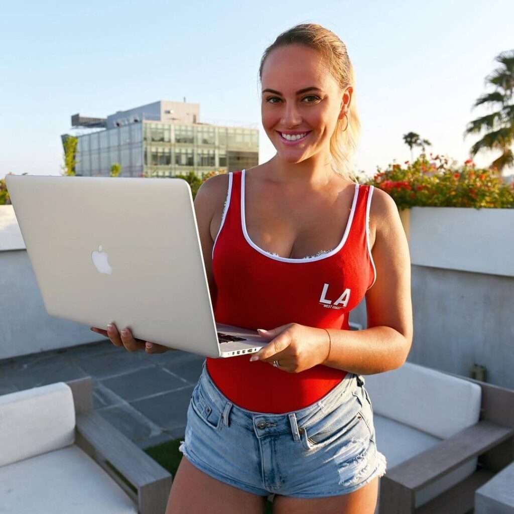 Biancadata in a red tank top pair with denim shorts while holding a macbook in her hand