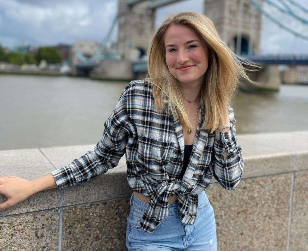 Änna Sophie is poses for a photo while wearing a dress shirt with jeans and smiling towards camera