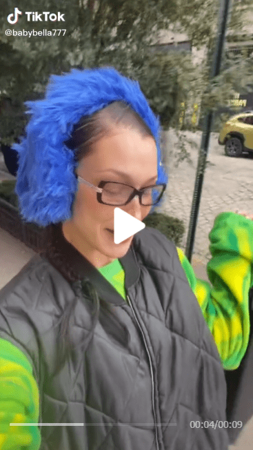 Bella Hadid in a blue hair dye and black coat while making a TikTok video
