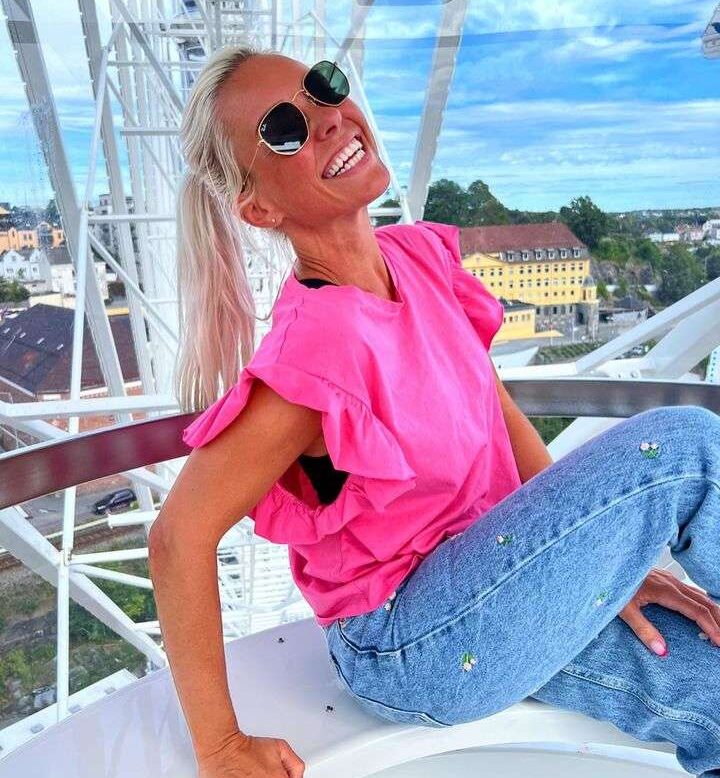 Camilla Annaniassen in a pink top with blue jeans with black goggles while poses for a photo