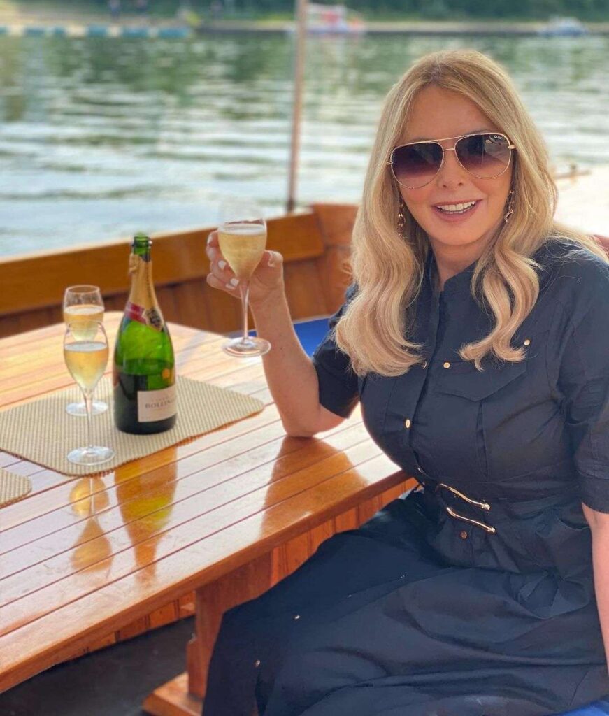 Carol Vorderman holding a glass of wine in her hand while wearing a sexy black outfit