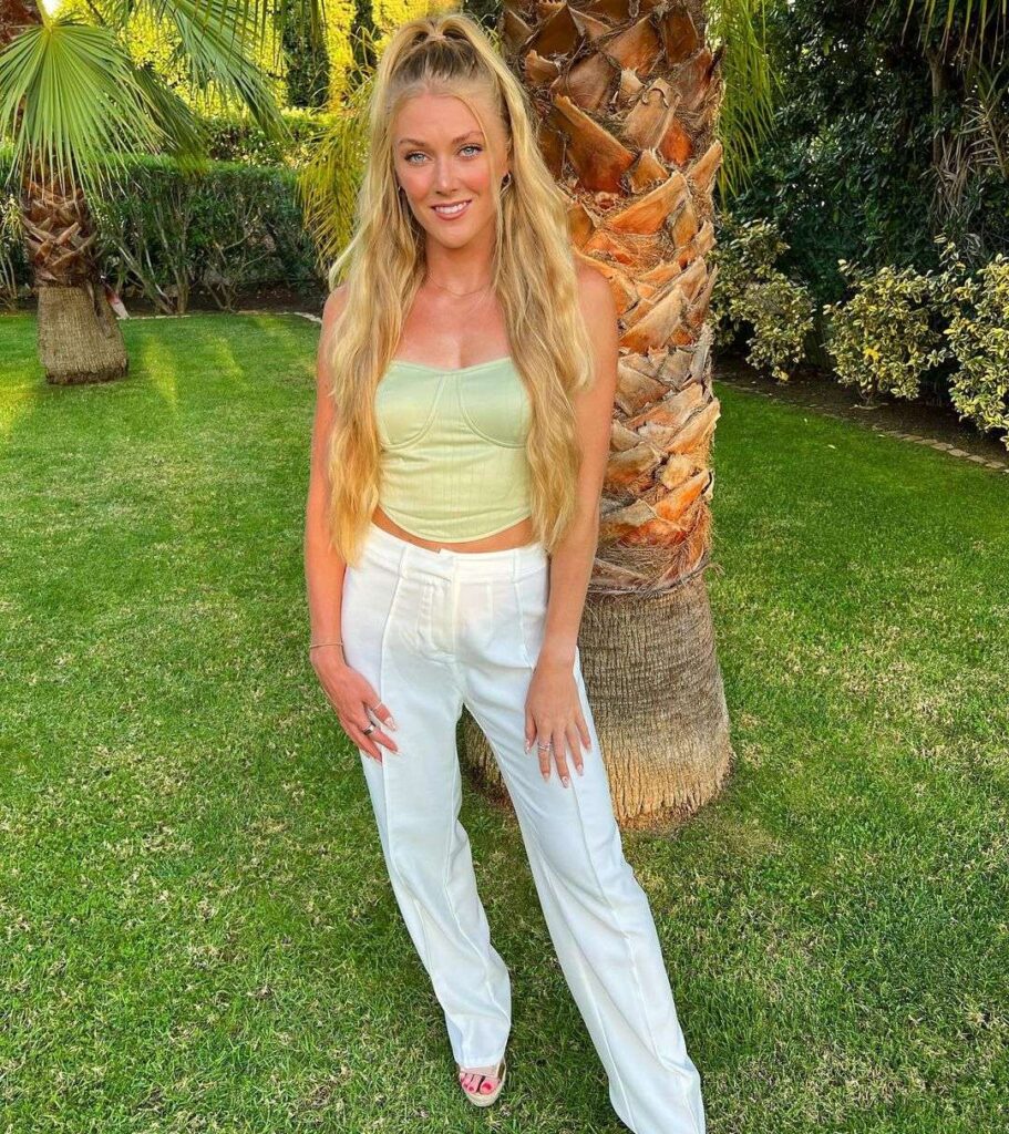 Ellie Baker in a green off shoulder top with white pants while poses for a photo