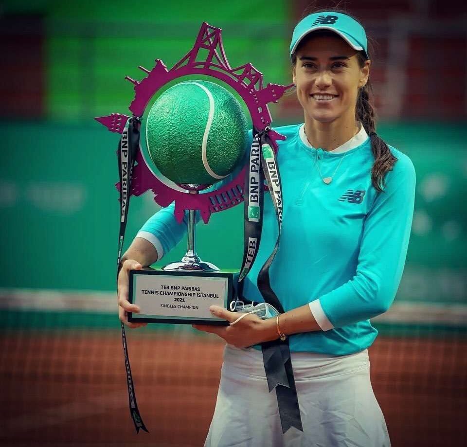 Sorana Cirstea in a turquoise-blue tennis costume while holding her tennis championship trophy and poses for a photo