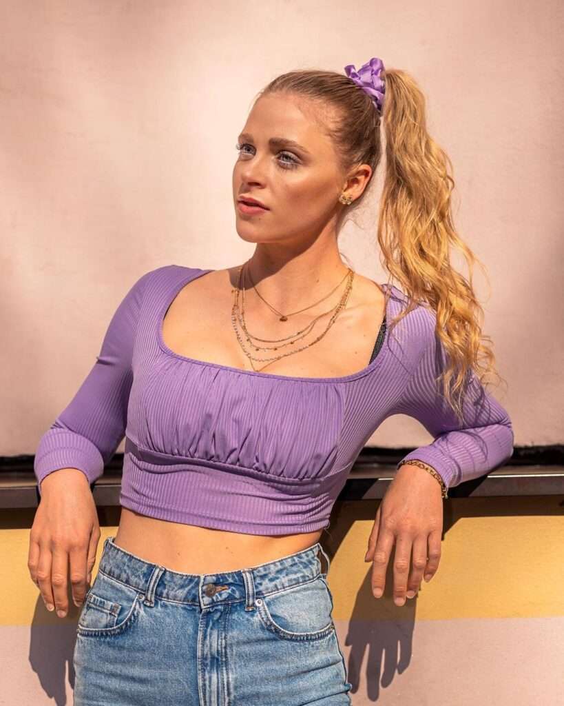 Svenja Sommer in a purple crop top pair with denim pants and layered necklace while poses for a photo