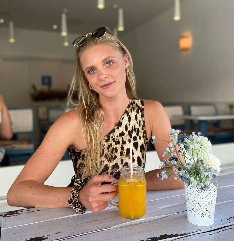 Svenja Sommer in a sleeveless top with matching scrunchie holding a glass of fresh juice in her hand and smiling towards camera