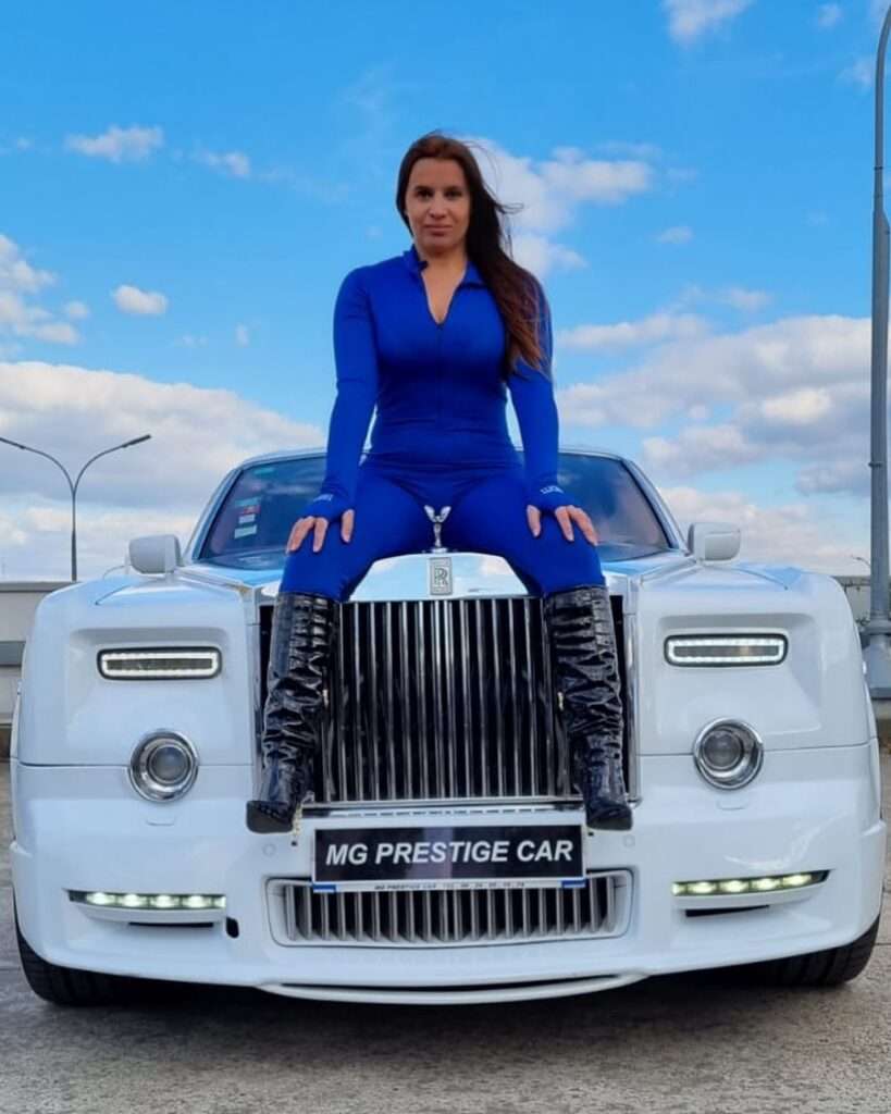Bestone Paris is sitting on a car while wearing a royal blue legging two piece suit showing her figure.