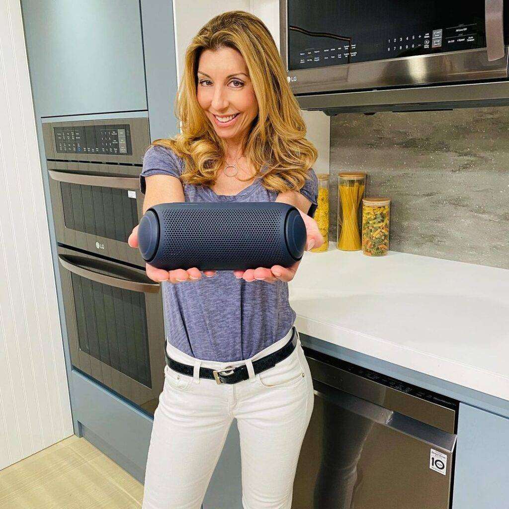 Cook With Shereen is just posing for a picture while showing a gadget and wearing pant-shirt.