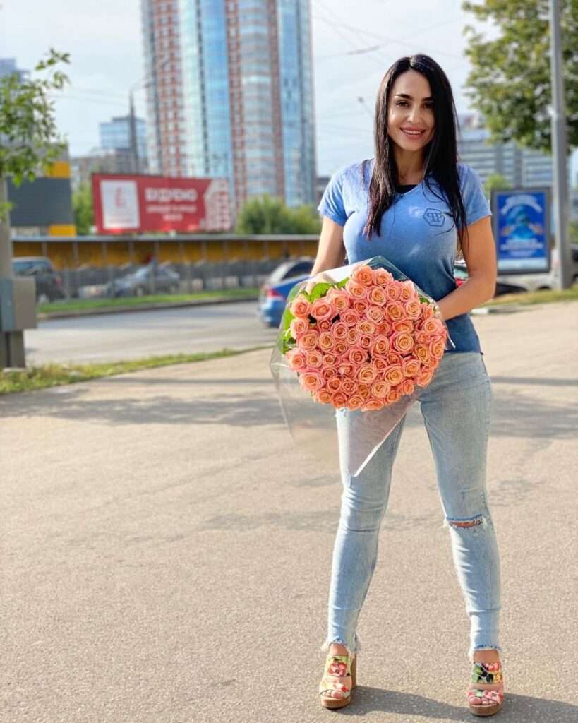Demidova Helenka is holding a rose bookie on her birthday while wearing a shirt and jeans looking stunning.