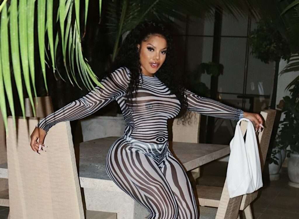 Holly in the black and grey printed jumpsuit pair with black sandals while sitting on the table