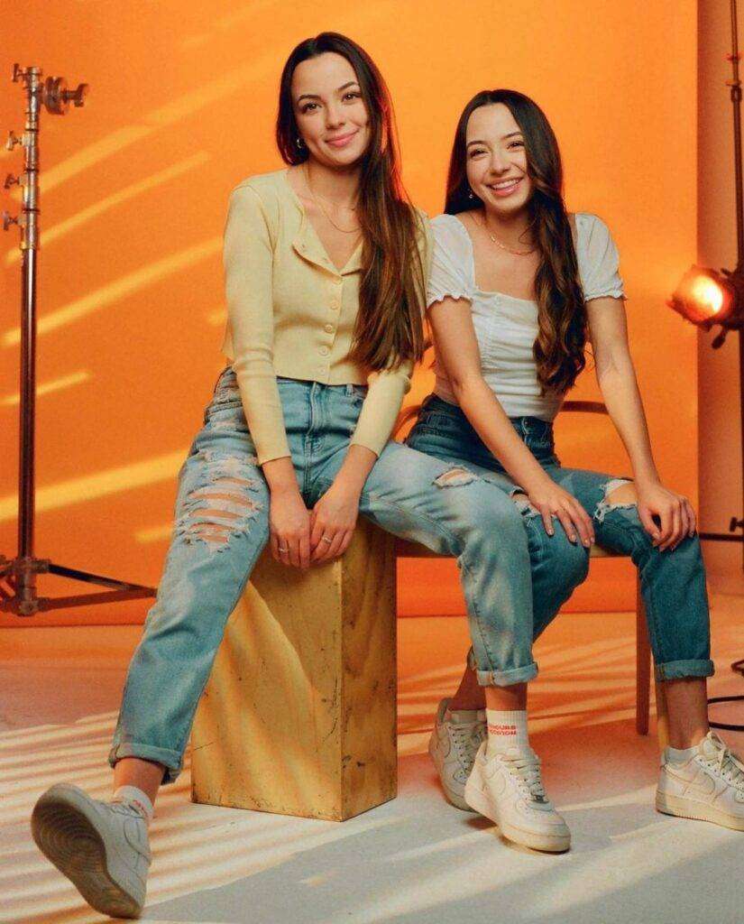 Merrell Twins are sitting in studio and giving pose for a picture as they looks crazy and beautiful while Vanessa wearing a check shirt with pant and joggers and Veronica wears shirt with pant.