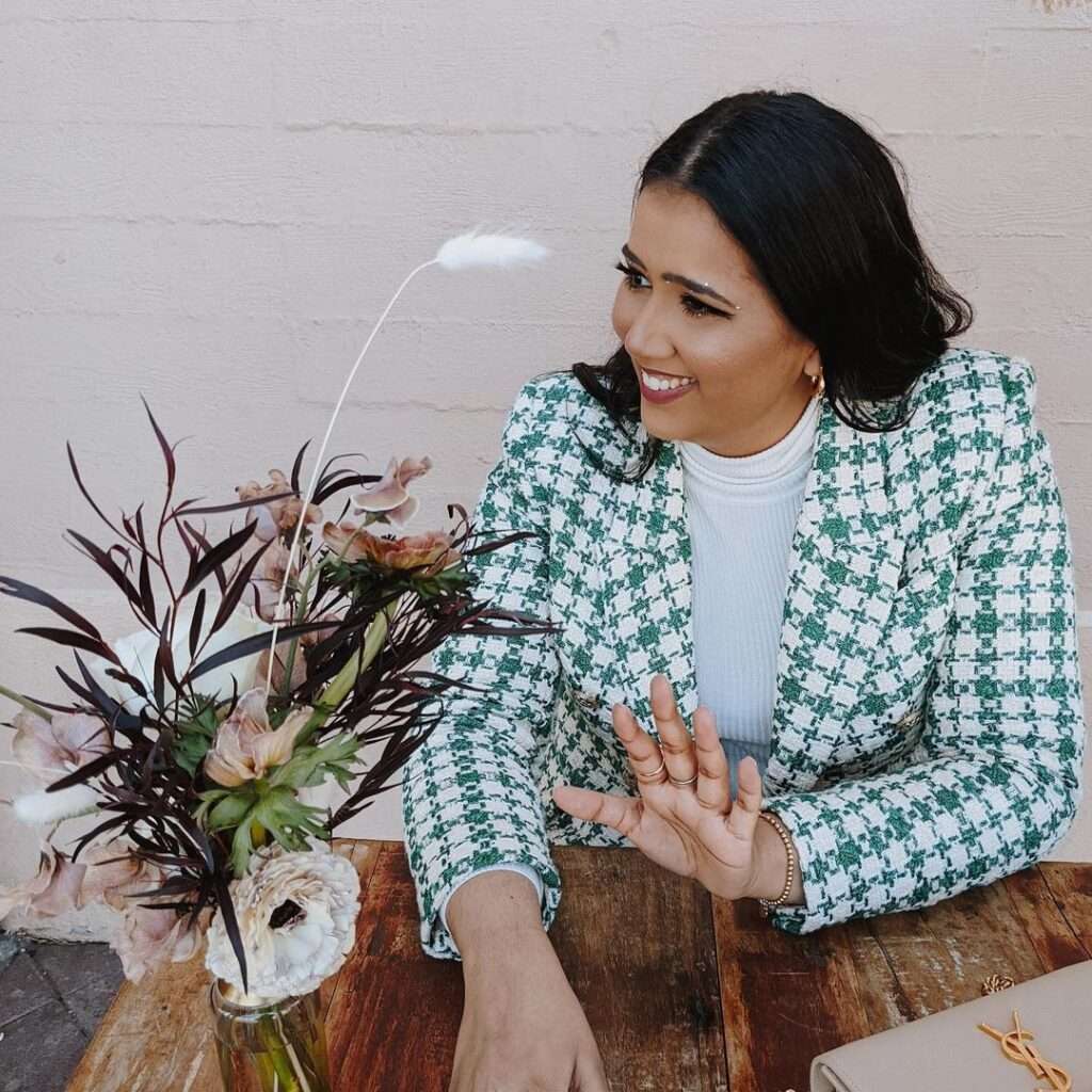 Shreyacooks is giving a cute smile as she is posing for a picture while wearing a coat and pant-shirt.