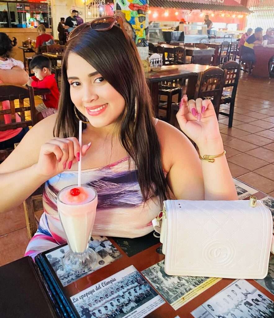 Abril Figueroa is taking a fruit dink while sitting in a cafe and wearing a multi-shade tie and die bodycon