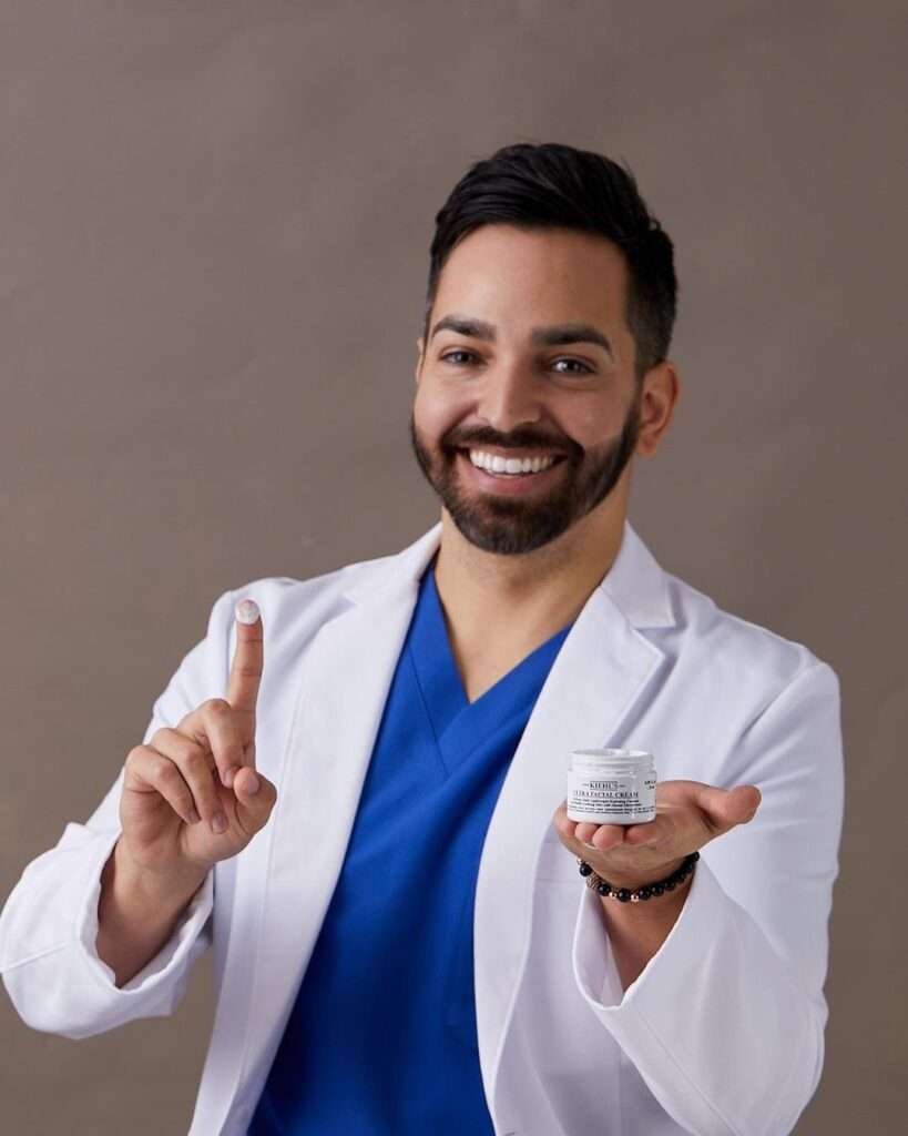 Dr. Muneeb Shah in the blue shirt with white coat while showing a skin care product