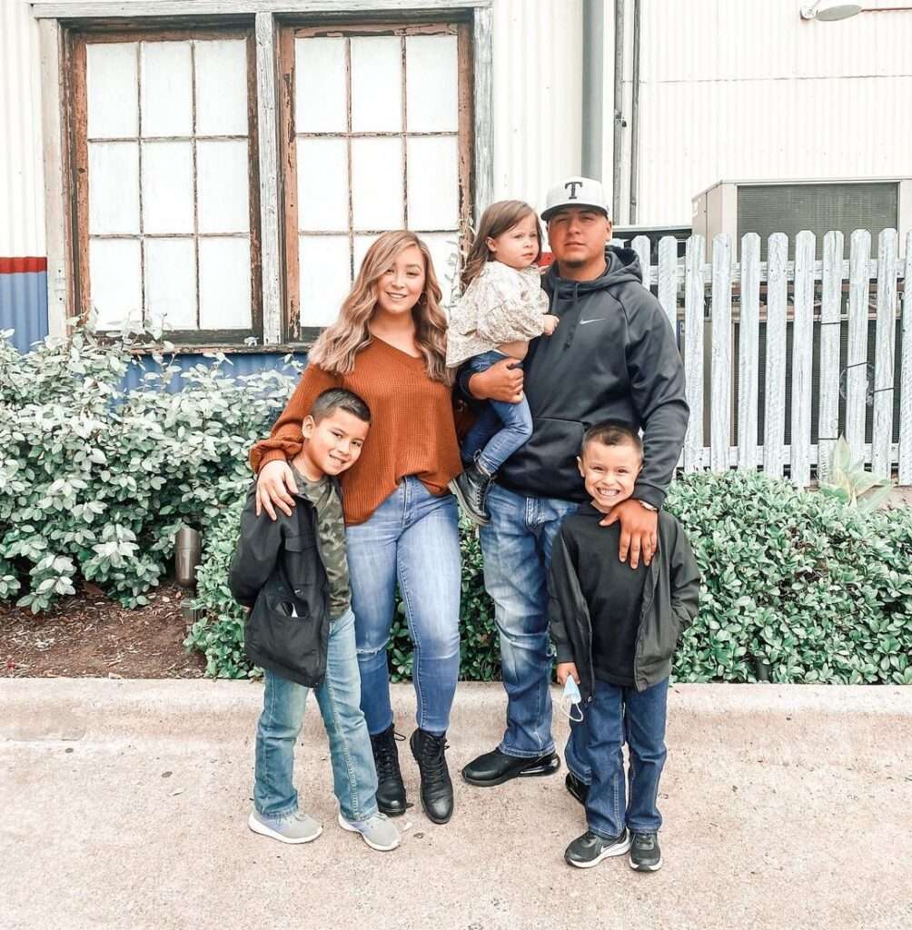 Elizabeth Salazarrr is just posing for a picture with her family while wearing a pant-shirt looking happy.