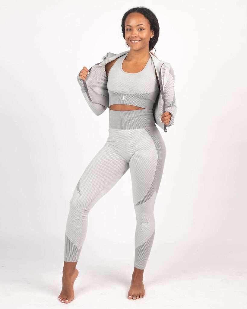 Jenn Ram is standing while wearing a gym suit and is smiling and posing for a picture.