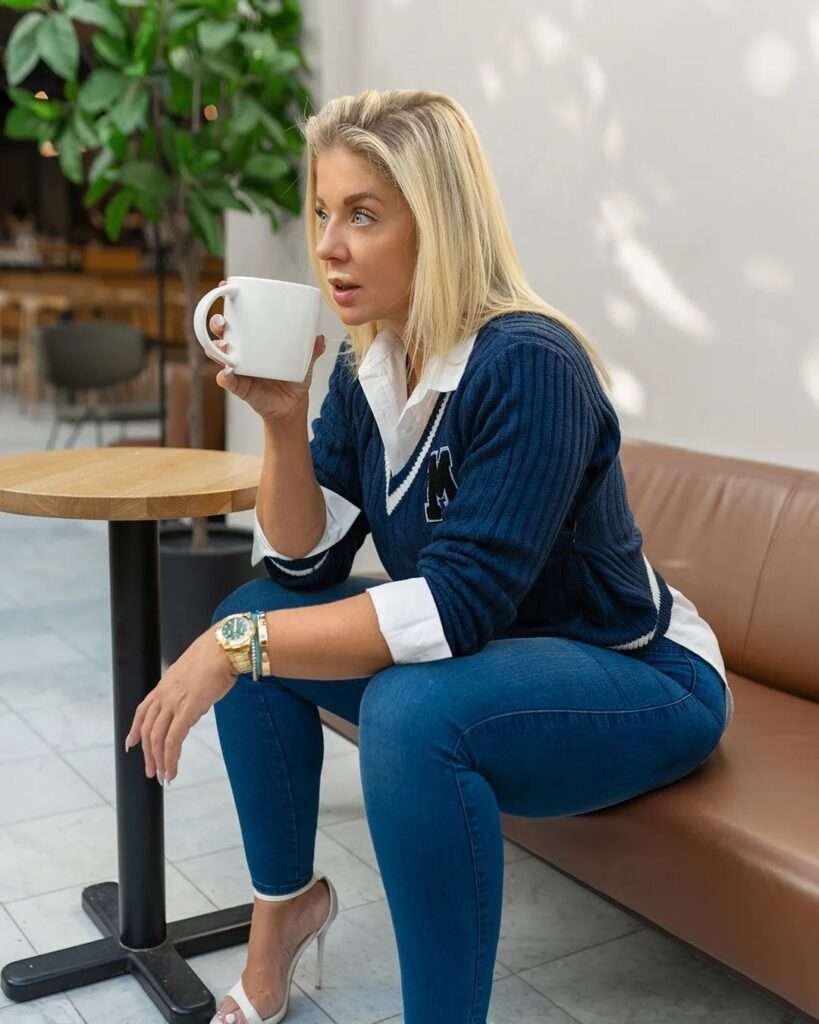 Mia Sand is drinking coffee and is posing for a picture while wearing a shirt with blue jeans.