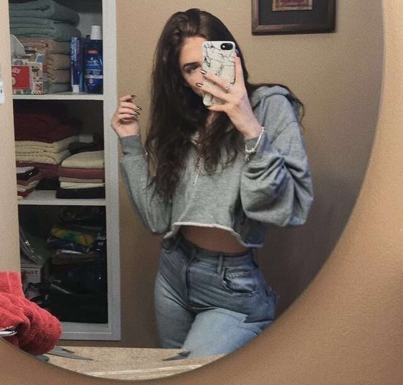 Paige Mousseau in the grey hoodie pair with blue jeans while taking a photo in the front of mirror