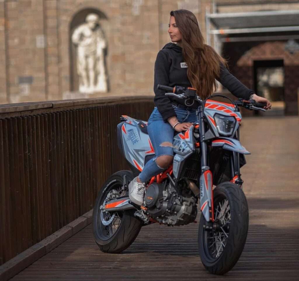 sumozopfie is showing her jawline towards camera while sitting on the sports bike and wearing a black hoodie with blue jeans