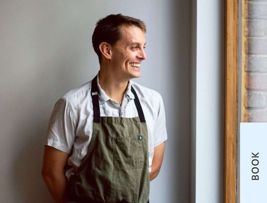 Thomas Straker is just posing for a picture and laughing while wearing an apron.