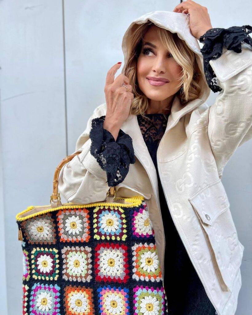 Barbara D'Uro is wearing black shirt over white jacket and holding colourful purse and posing for the picture