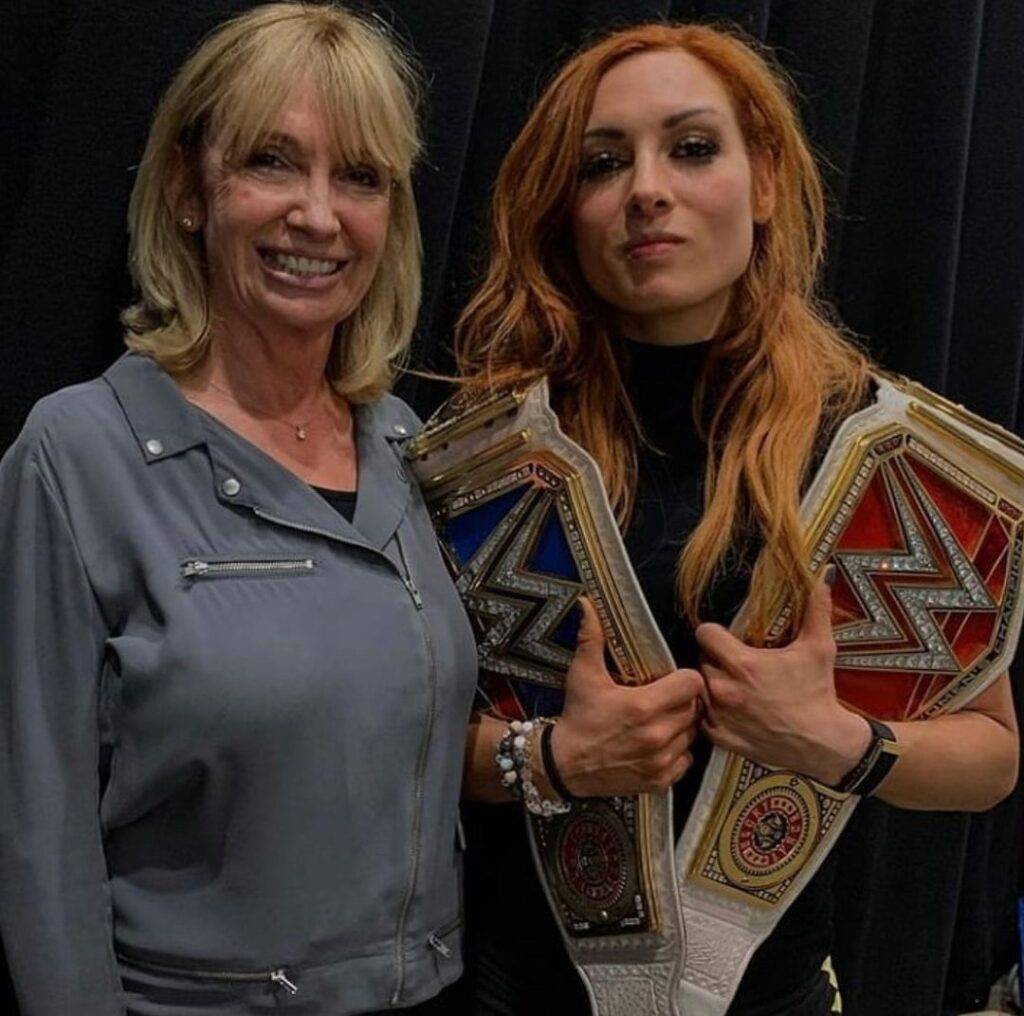 Becky Lunch is holding the WWE belts and standing with her mom and posing for the picture