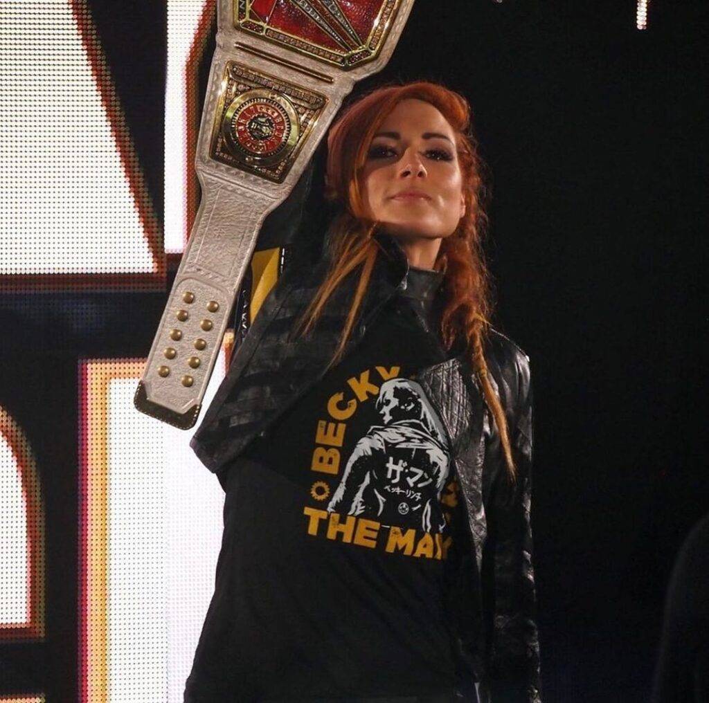 Becky Lynch is showing her WWE belt and wearing black jacket and posing for the picture