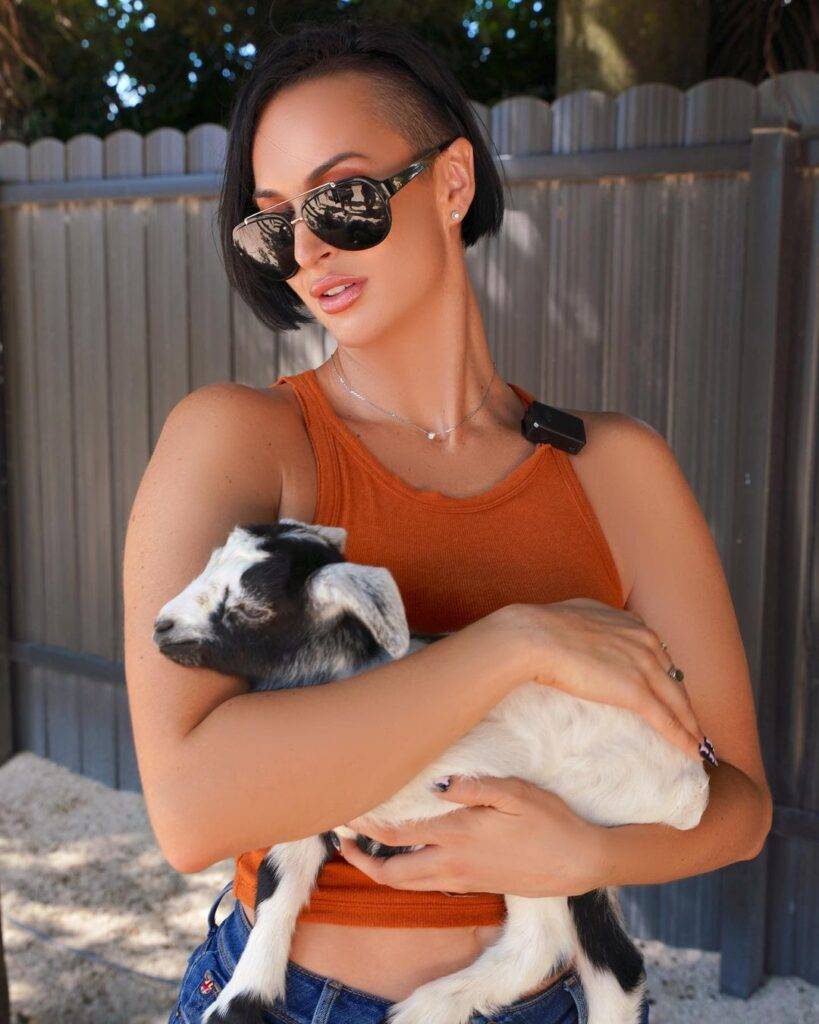 Zahra Elise is wearing the orrage dress, black glasses or holding goat's child and posing for the picture