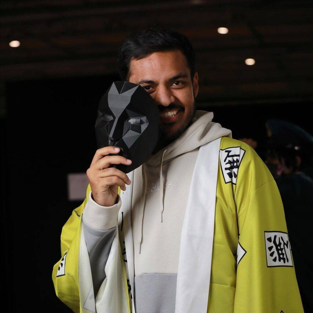 BanderitaX in the off white hoodie with a printed shrug while smiling towards camera