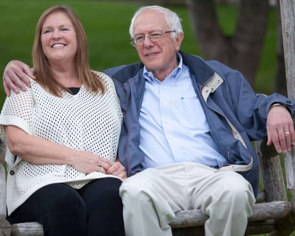 Bernie Sanders is sitting with his wife and is posing for a picture while smiling.