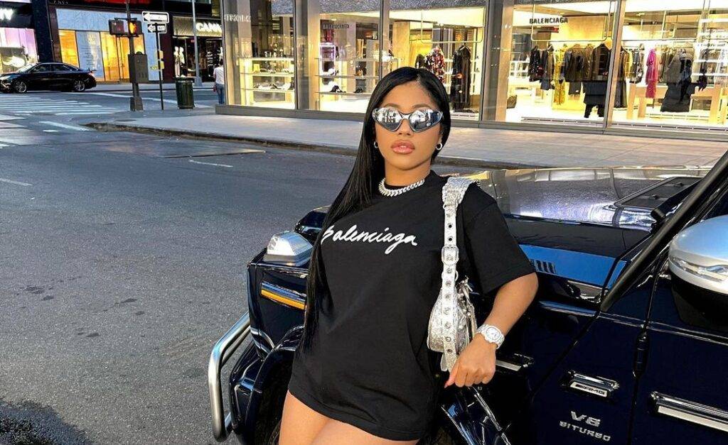 Hennessy Carolina in the black t-shirt pair with a white bad and shades while taking picture along her car