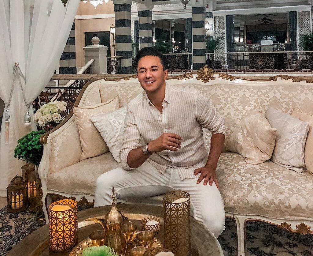 RedOne is looking handsome in the dress shirt and matching pants while sitting in his home's drawing room and poses for a photo