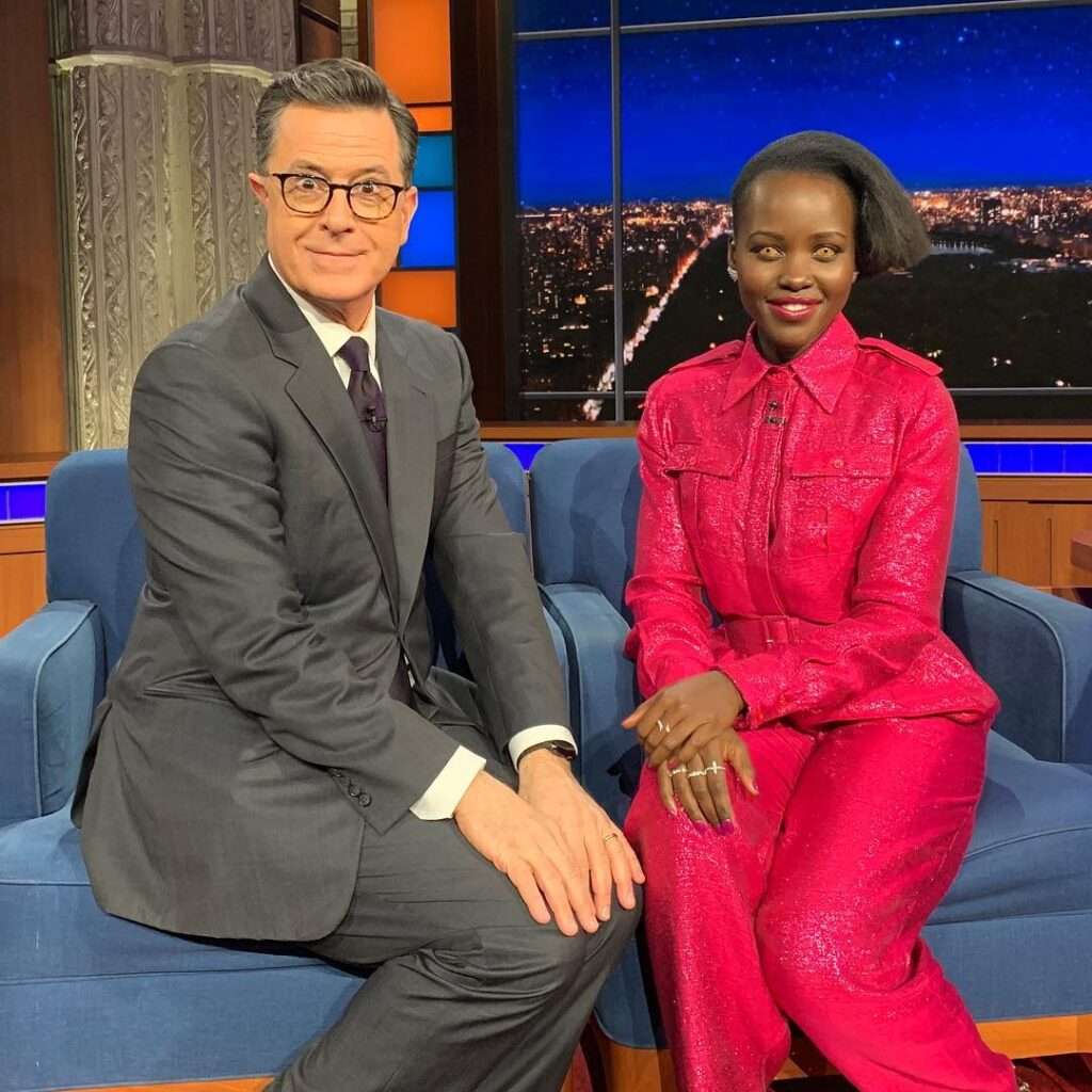 Stephen Colbert is posing for a picture while sitting with a celebrity in a show.