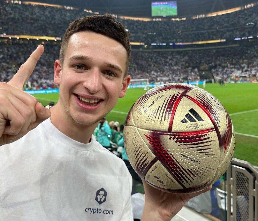 Theo in the white shirt while smiling towards camera and holding a football in his hand